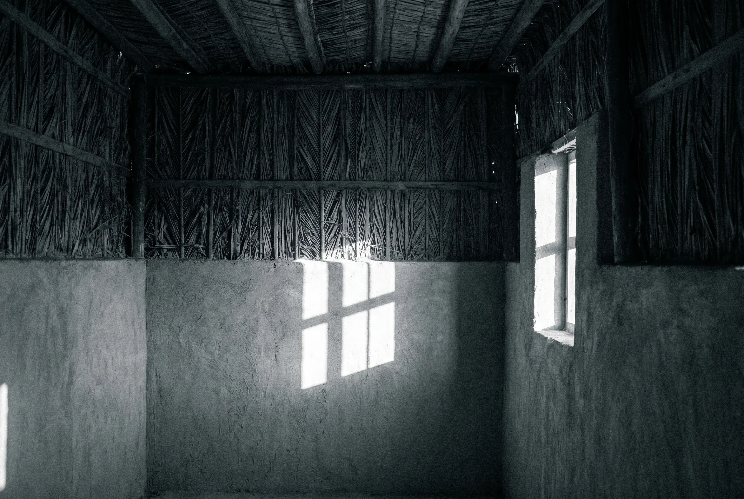 Hard daylight falling across the bare wall of a traditional Emirati interior